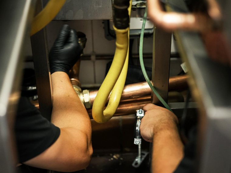 GreaseTech engineer working on kitchen pipework beneath a sink